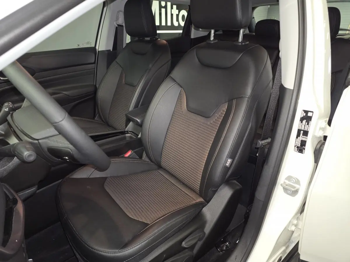 Vue intérieure côté conducteur du Jeep Compass blanc 2024, sièges noirs en tissu et cuir avec surpiqûres bronze.