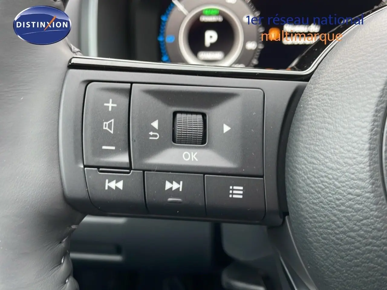 Gros plan sur les commandes multifonctions gauche du volant du Nissan Qashqai blanc nacré 2025 avec affichage digital en arrière-plan.