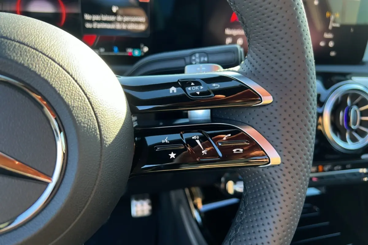 Gros plan sur le volant cuir perforé de la Mercedes Classe A 200D BVA Exclusive Design noir cosmos, avec commandes multifonctions.