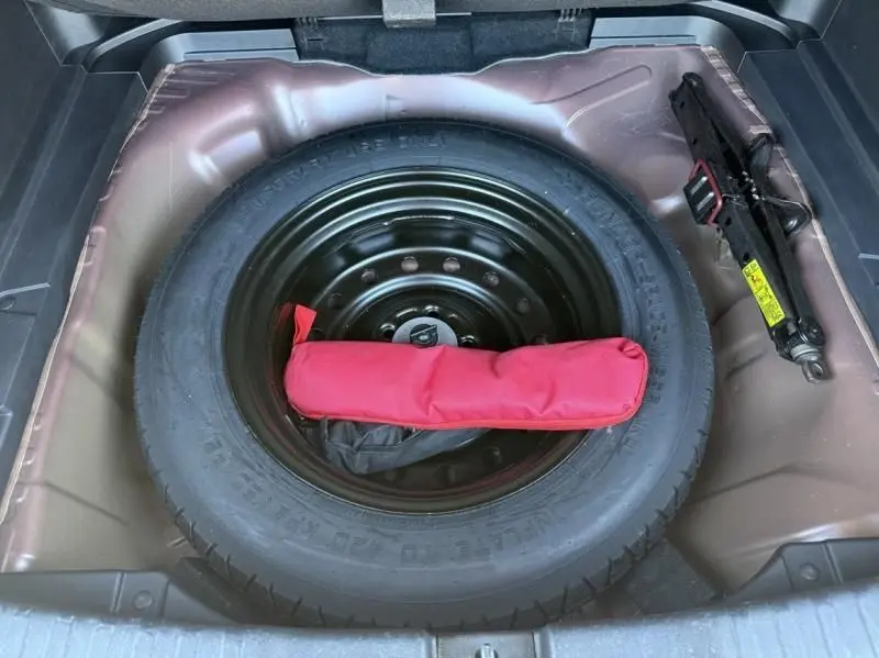 Vue plongeante sur la roue de secours noire et le cric dans le coffre d'un Honda CR-V rouge métal 2017.