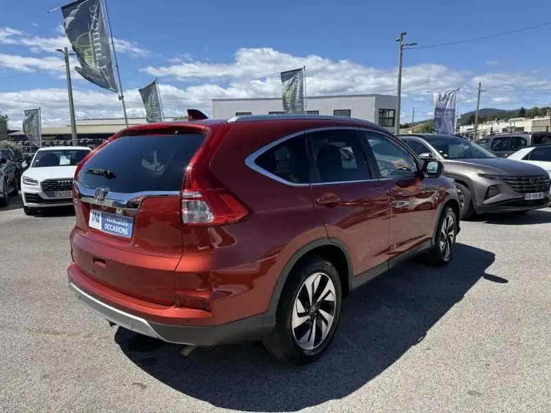 Vue 3/4 arrière droite du Honda CR-V rouge métal 2017 avec jantes alliage et vitres teintées, stationné en extérieur.