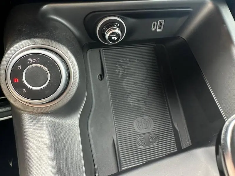 Gros plan sur la console centrale noire de l'Alfa Romeo Tonale avec molette de sélection de mode et prise 12V visible.
