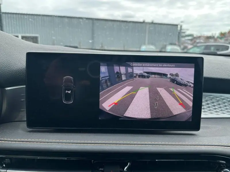 Écran tactile intérieur montrant la caméra de recul d'une Alfa Romeo Tonale blanche, vue depuis le tableau de bord.