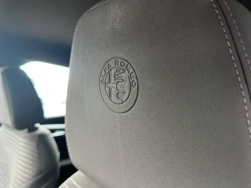 Gros plan sur l'appui-tête avant en cuir noir avec logo Alfa Romeo embossé, intérieur du Tonale 2025.