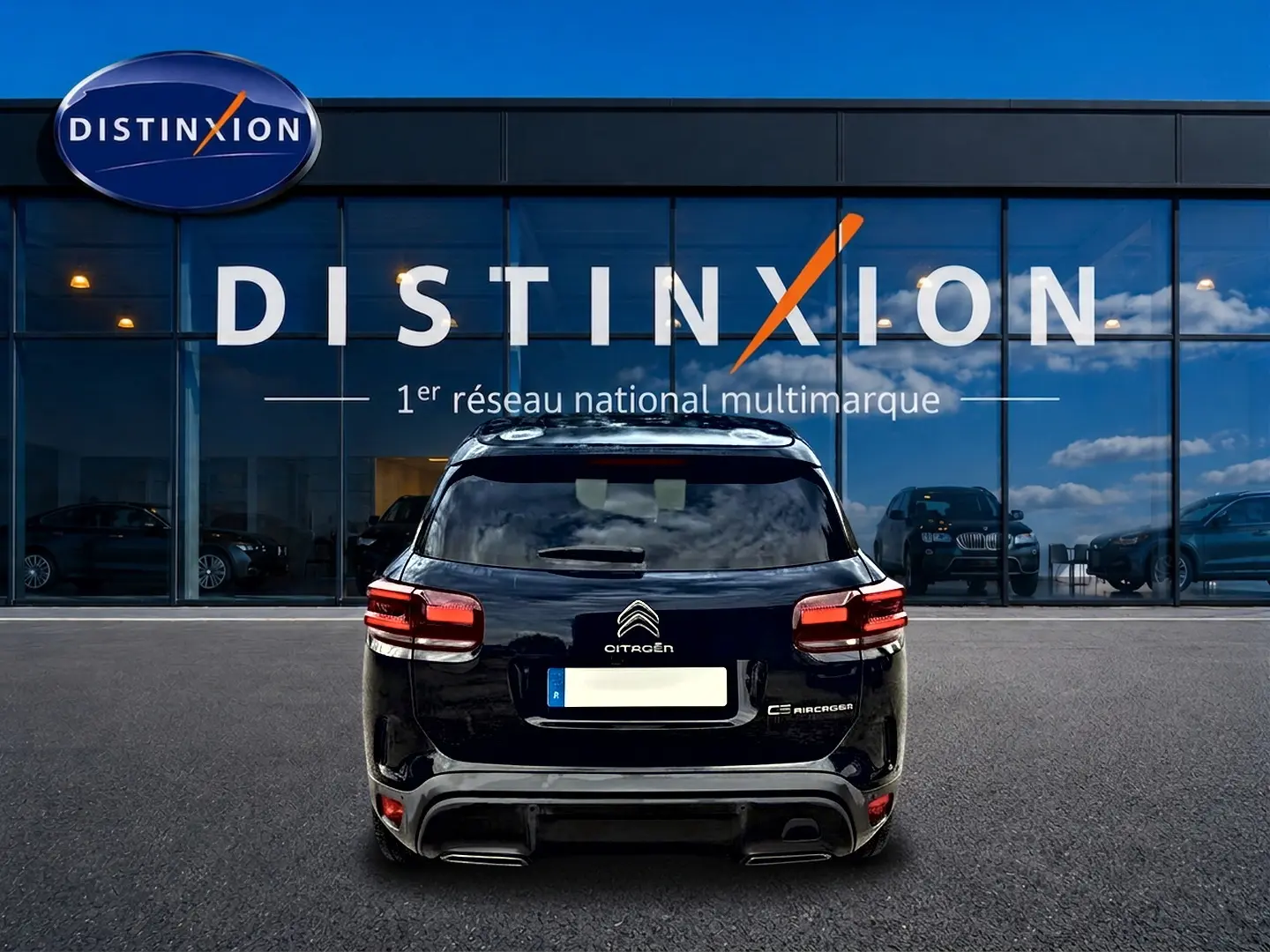 Vue arrière d'un Citroën C5 Aircross noir 2024 garé devant une vitrine avec logo Distinxion.