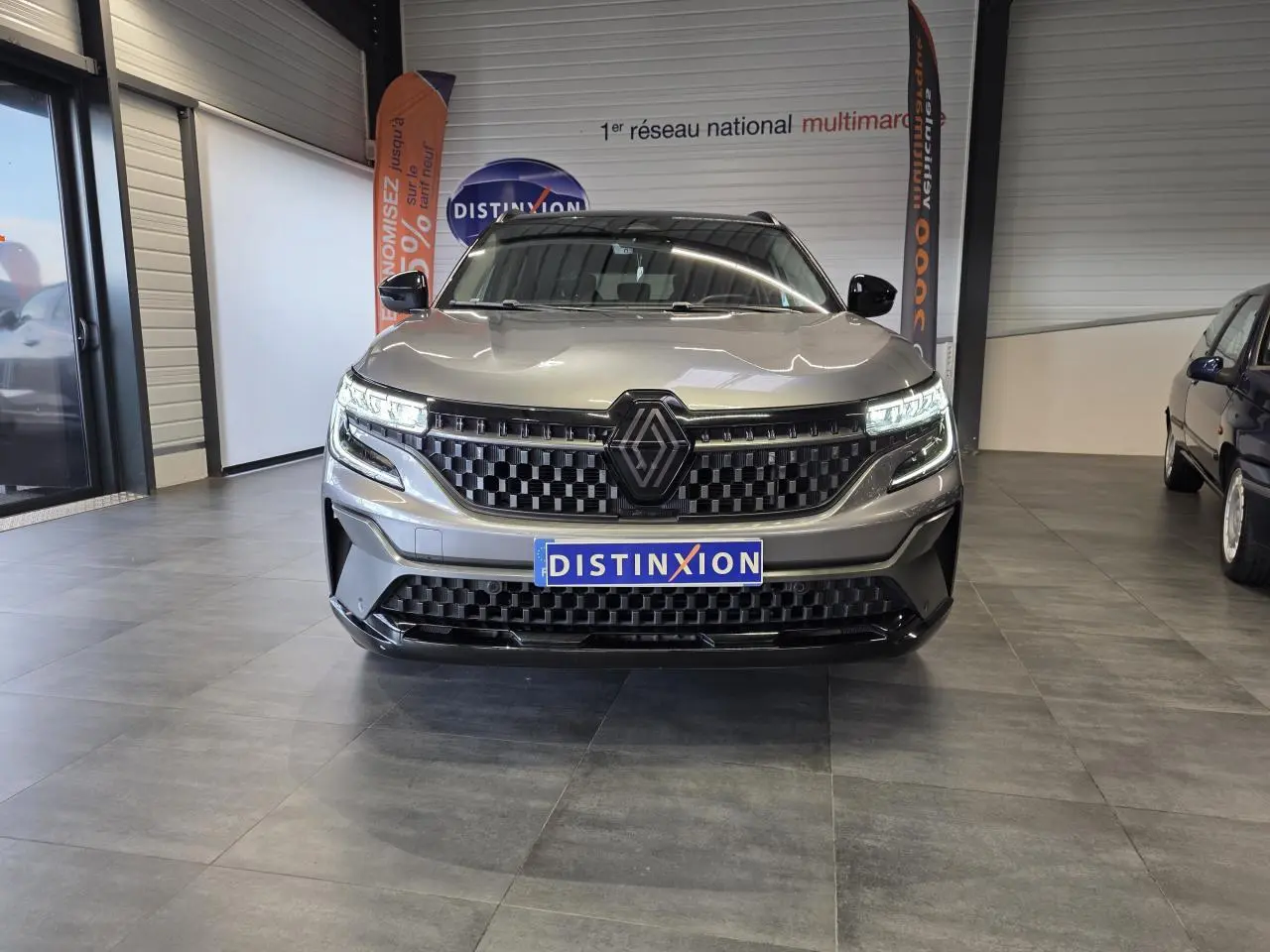 Vue de face du Renault Austral gris foncé avec calandre damier ice black et feux LED allumés en showroom.