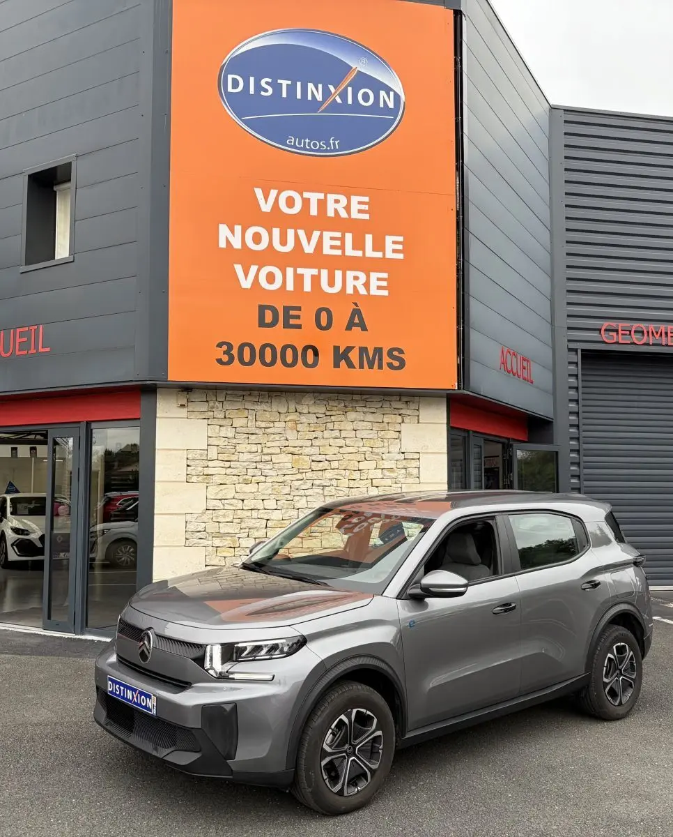 Vue 3/4 avant droite d'un Citroën C3 Aircross électrique gris foncé garé devant un bâtiment commercial.