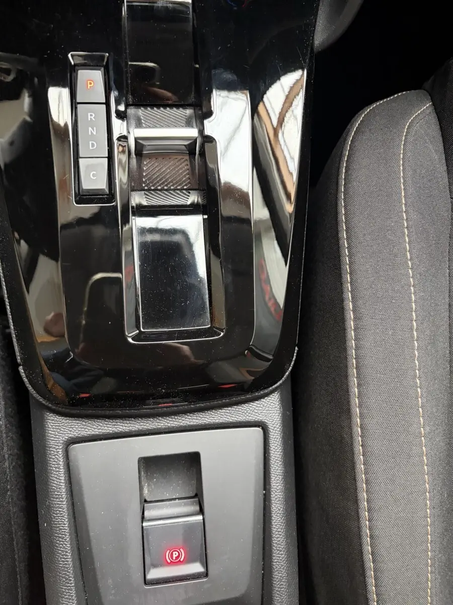 Gros plan sur la console centrale noire brillante avec levier de boîte auto et frein à main électrique, siège tissu gris visible.