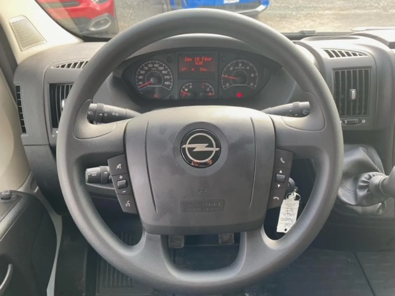 Vue rapprochée du volant noir d'un Opel Movano Fourgon blanc, avec commandes intégrées et tableau de bord visible.