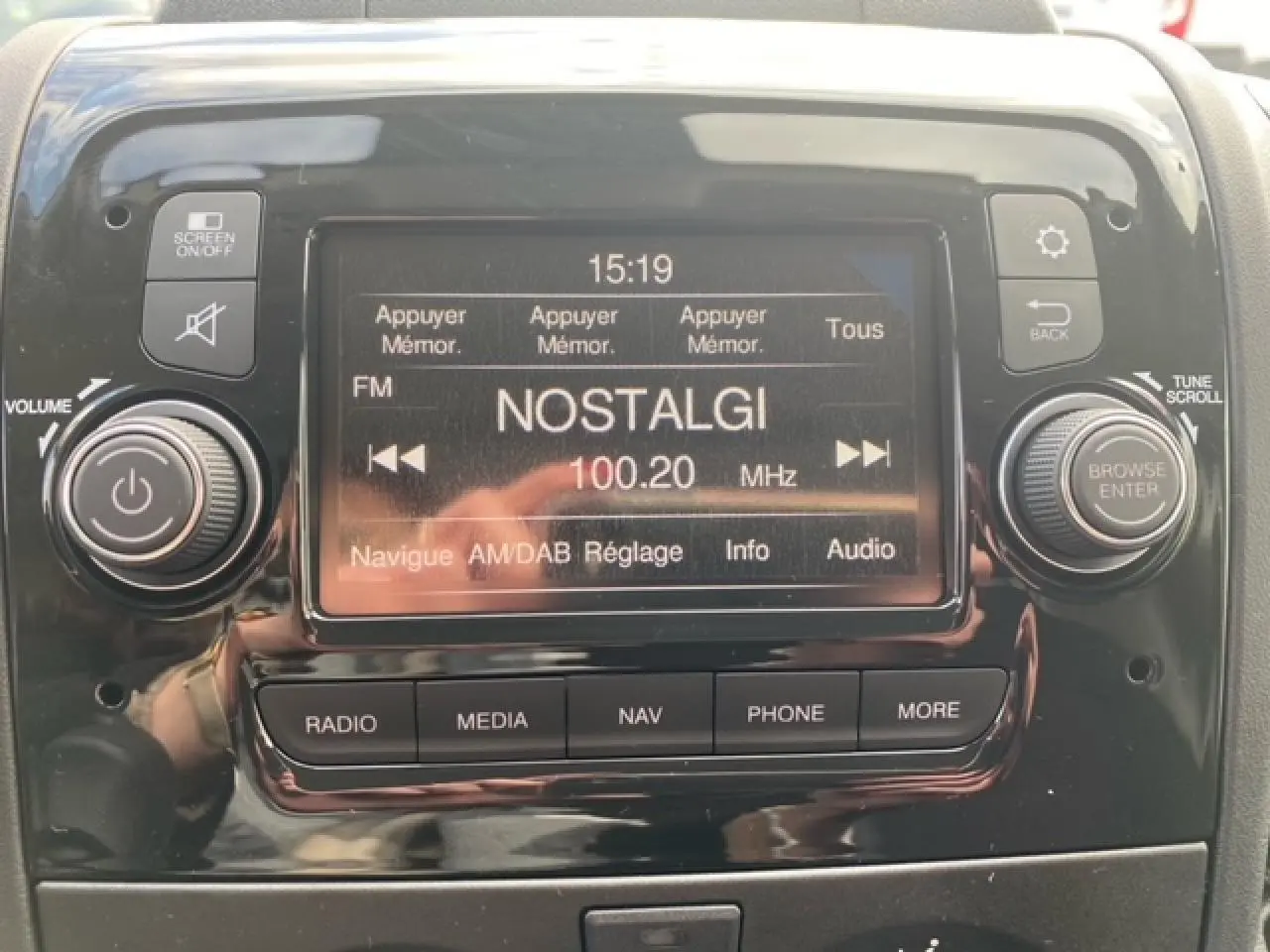 Détail de l'écran tactile central du système multimédia du fourgon Opel Movano blanc, affichant la radio FM sur la fréquence 100.20 MHz.