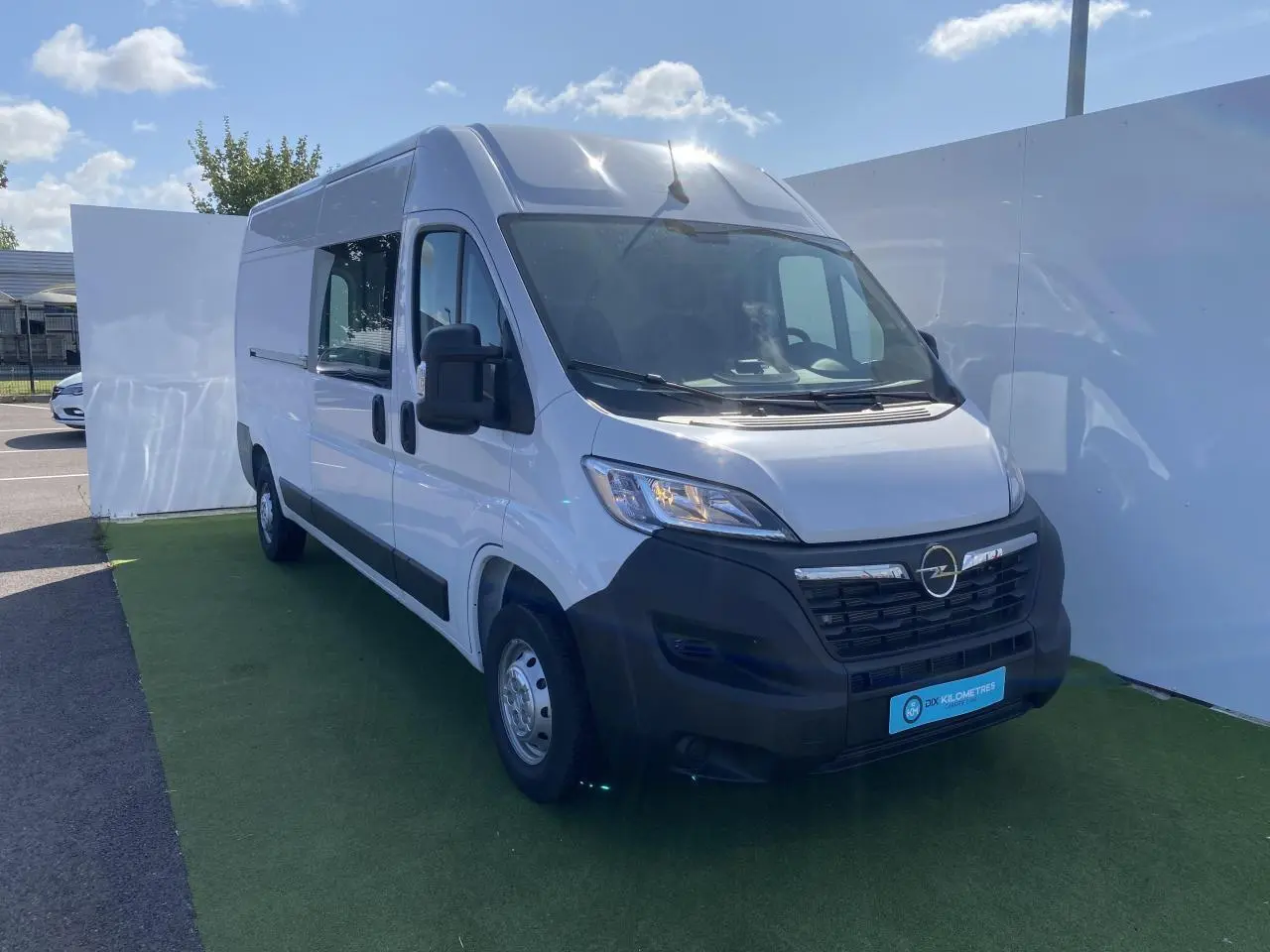 Vue 3/4 avant gauche d'un Opel Movano Fourgon blanc avec porte latérale vitrée et calandre noire.