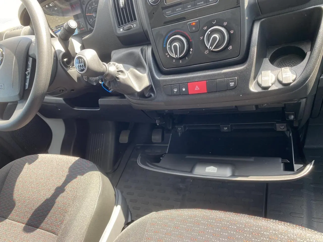 Intérieur Opel Movano Fourgon 2023 vu côté passager, tableau de bord noir avec boîte à gants ouverte et levier de vitesses manuel.