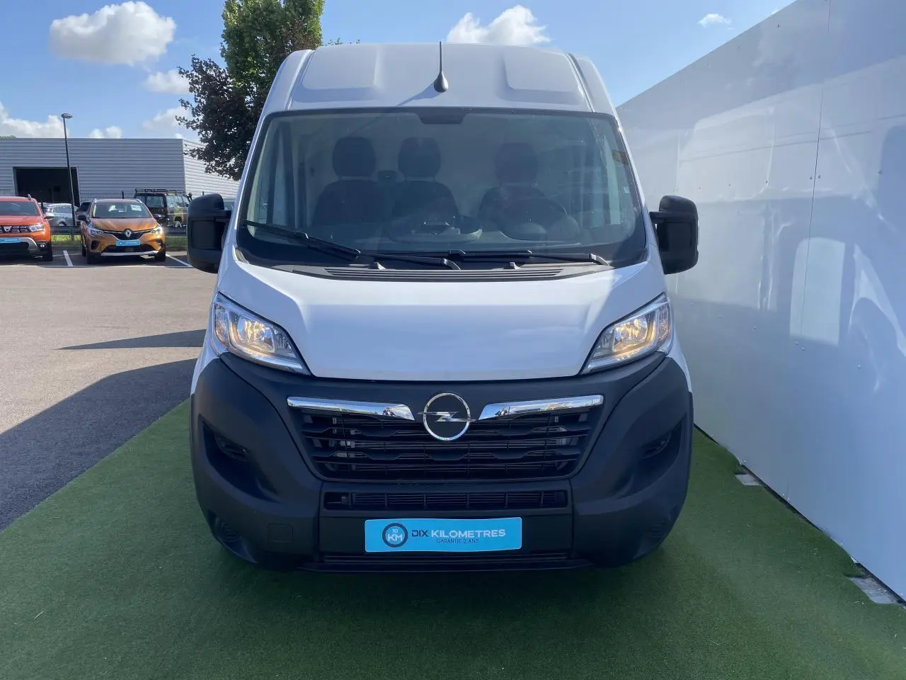 Vue frontale d'un Opel Movano Fourgon blanc 2023 avec calandre noire et logo Opel visible sur parking.