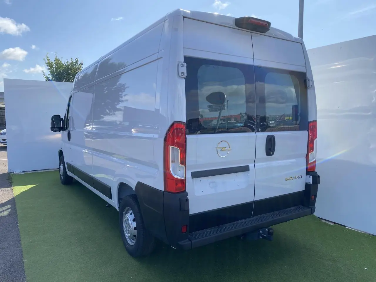 Vue 3/4 arrière droite d'un Opel Movano Fourgon blanc avec portes vitrées et crochet d'attelage visible.