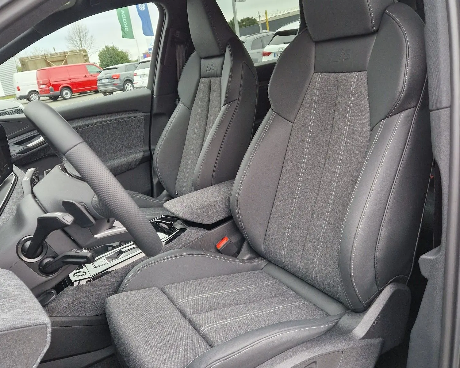 Vue intérieure côté conducteur de l'Audi Q6 e-tron Performance S-Line 2025 avec sièges sport gris Manhattan et surpiqûres contrastées.