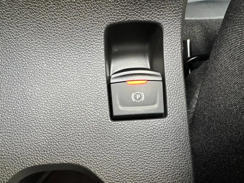Gros plan sur le bouton de frein à main électrique avec témoin rouge dans l'habitacle du Dacia Sandero 2025 gris Schiste métallisé.