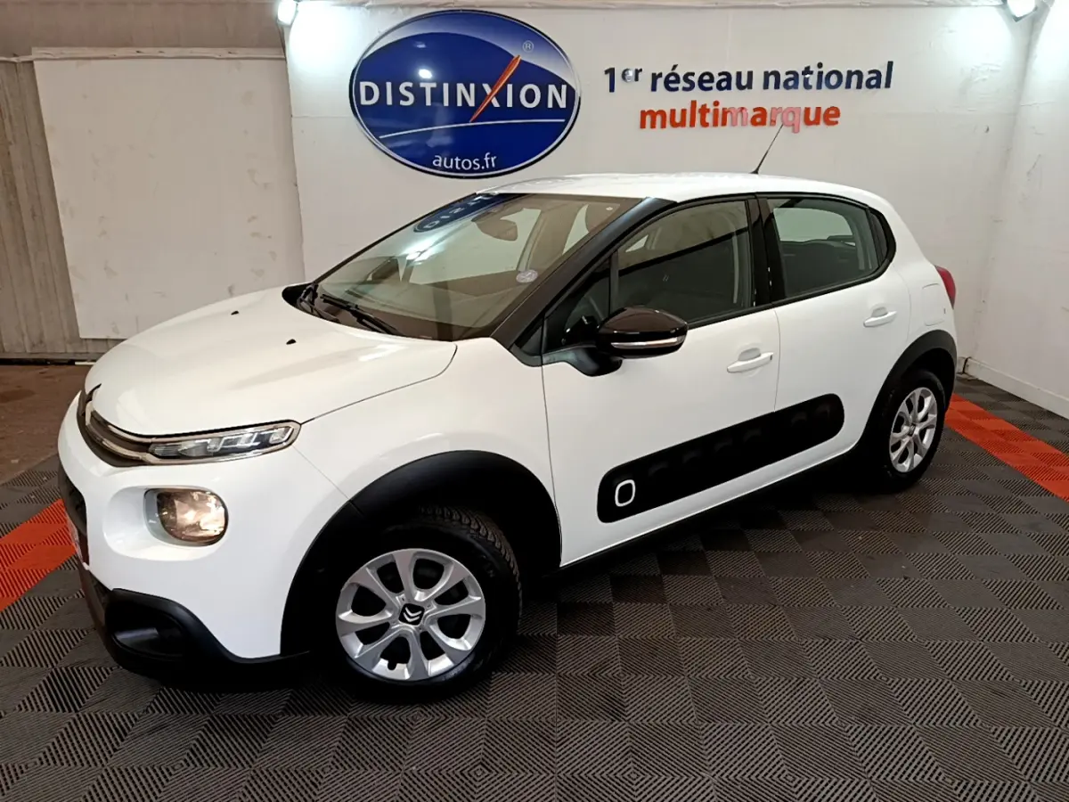 Citroën C3 blanche vue 3/4 avant droit, avec protections latérales noires et jantes alliage argentées.