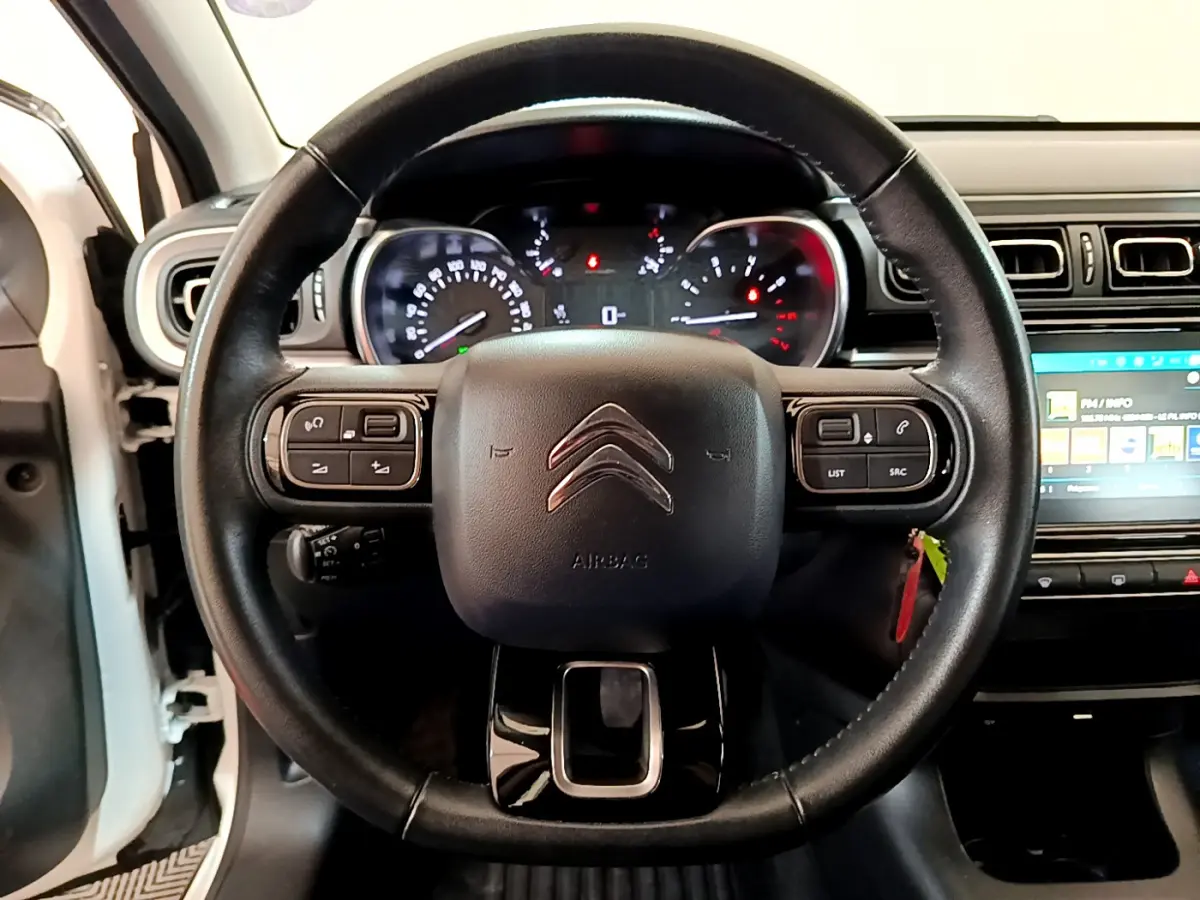 Vue rapprochée du volant cuir noir de la Citroën C3 blanche 2019 avec commandes intégrées et tableau de bord éclairé.