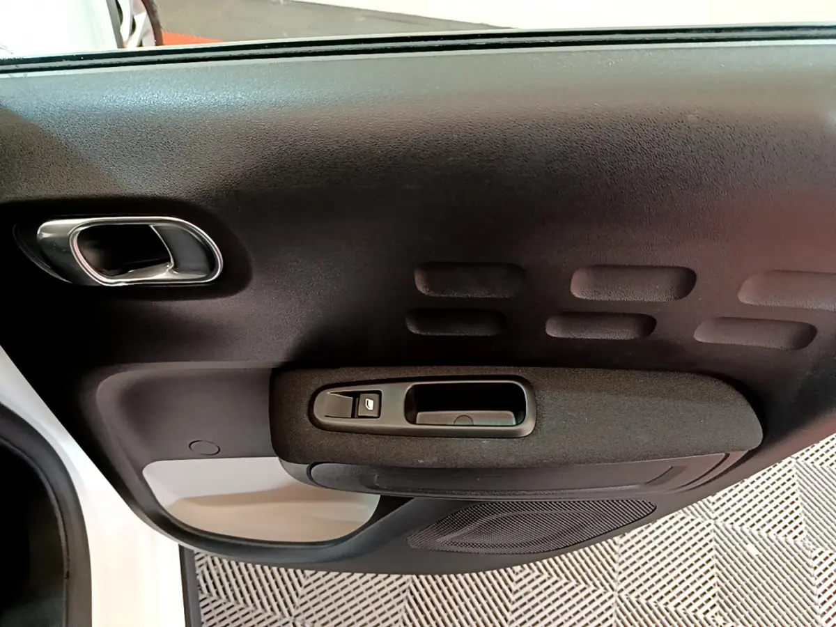 Gros plan sur la portière intérieure côté gauche d'une Citroën C3 blanche avec poignée et bouton de lève-vitre noir.
