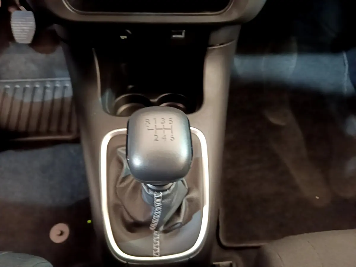 Le levier de vitesses manuel noir de la Citroën C3 blanche vu de dessus, entouré d'une garniture argentée.