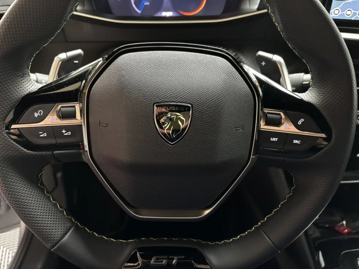 Gros plan sur le volant cuir et alu de la Peugeot 208 Hybrid 110 e-DCS6 GT avec logo lion et commandes intégrées.