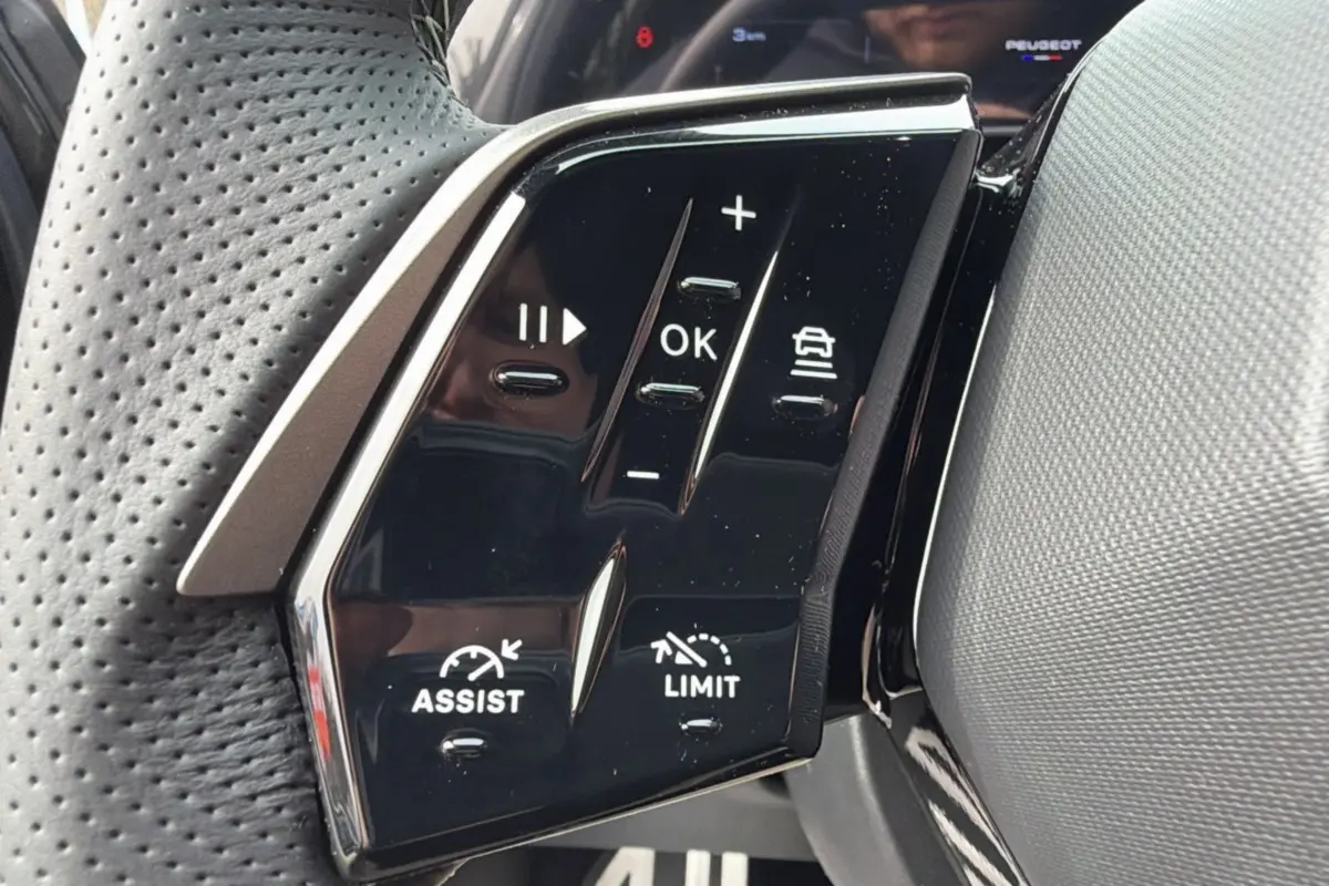 Gros plan sur les commandes multifonctions noires du volant cuir perforé du Peugeot 3008 Hybrid gris titane.