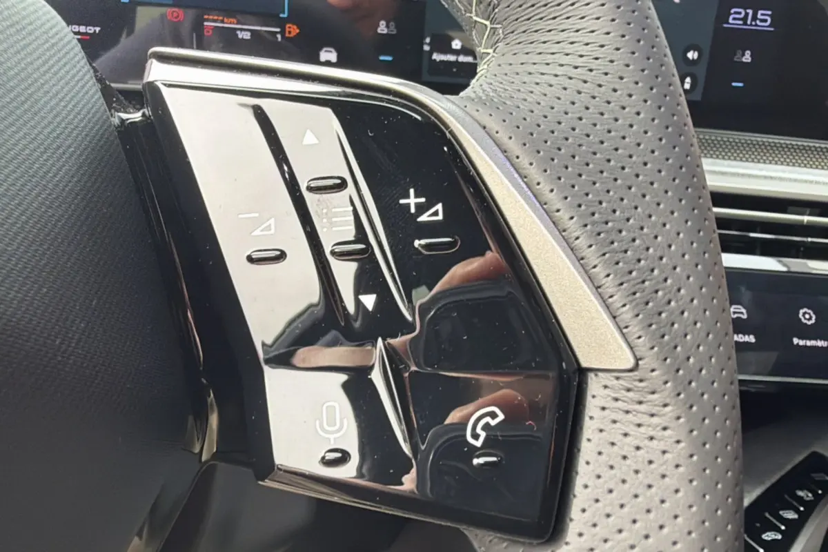 Gros plan sur les commandes noires brillantes du volant cuir perforé du Peugeot 3008 Hybrid gris titane.