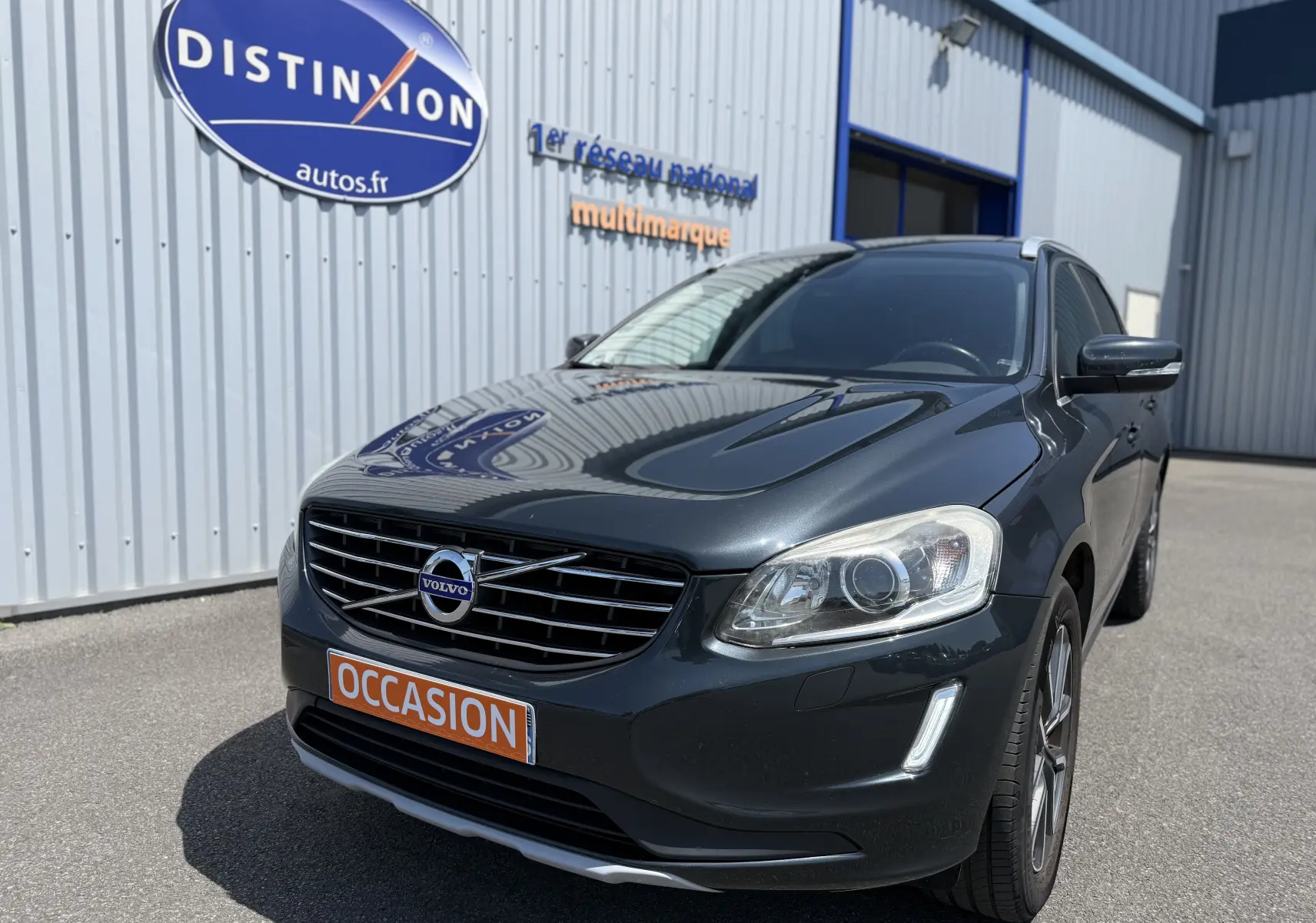 Volvo XC60 gris foncé en 3/4 avant droit, avec calandre distinctive et plaque orange "OCCASION" visible.