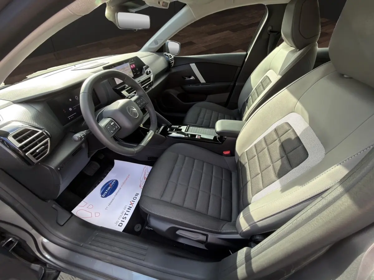 Vue intérieure côté conducteur de la Citroën C4 hybride 2025, sièges gris bi-ton et tableau de bord moderne avec écran tactile.