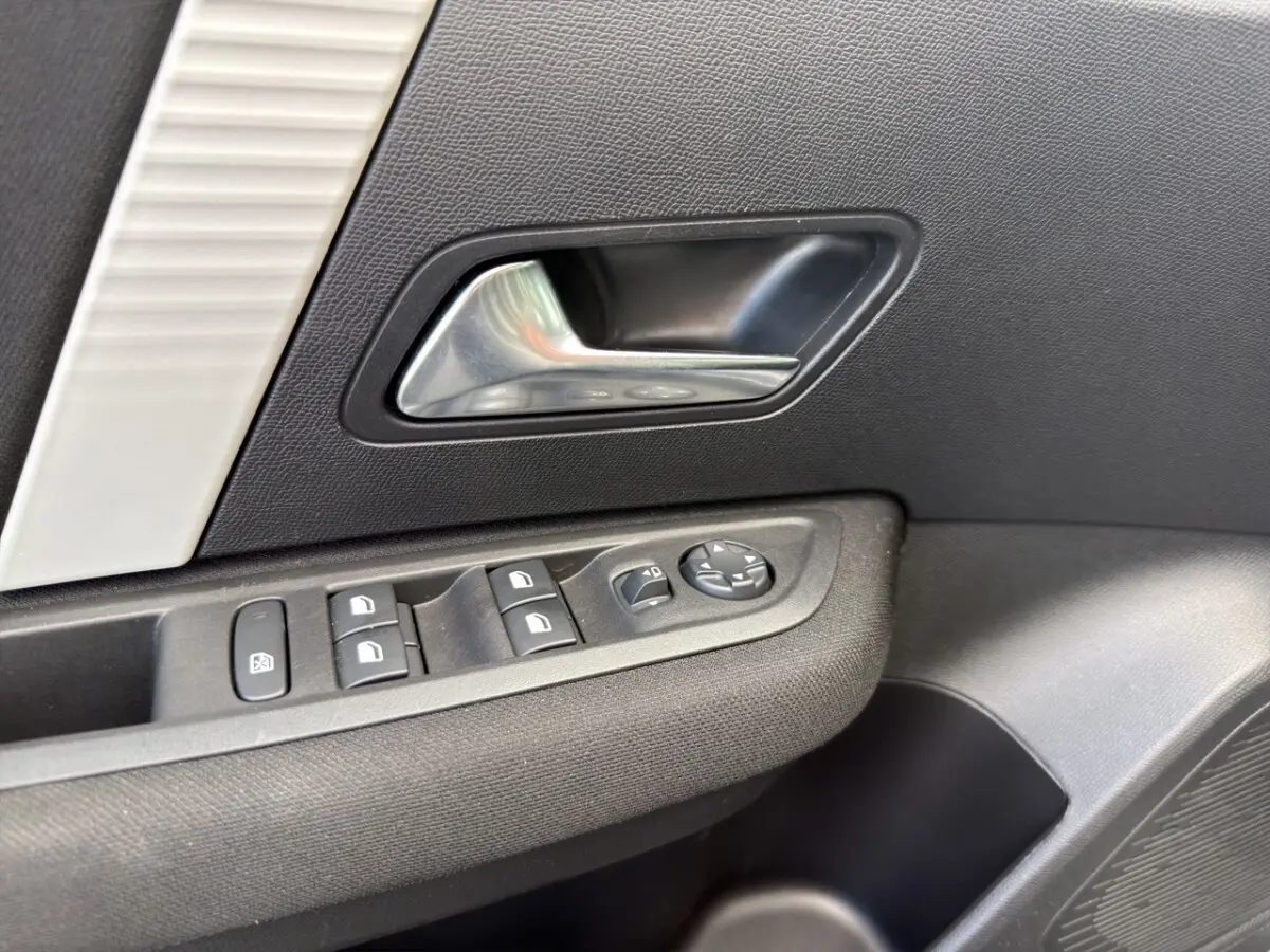 Gros plan sur la poignée intérieure et les commandes de vitres côté conducteur d'une Citroën C4 hybride 2025, finition gris foncé.