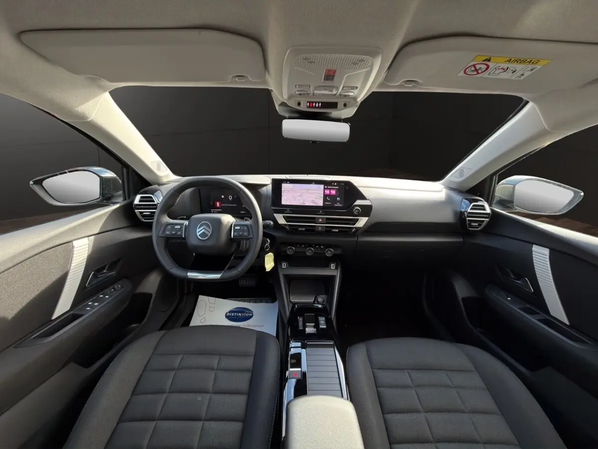Intérieur de la Citroën C4 Hybride 2025 vu de face, tableau de bord moderne avec écran tactile et sièges gris foncé.