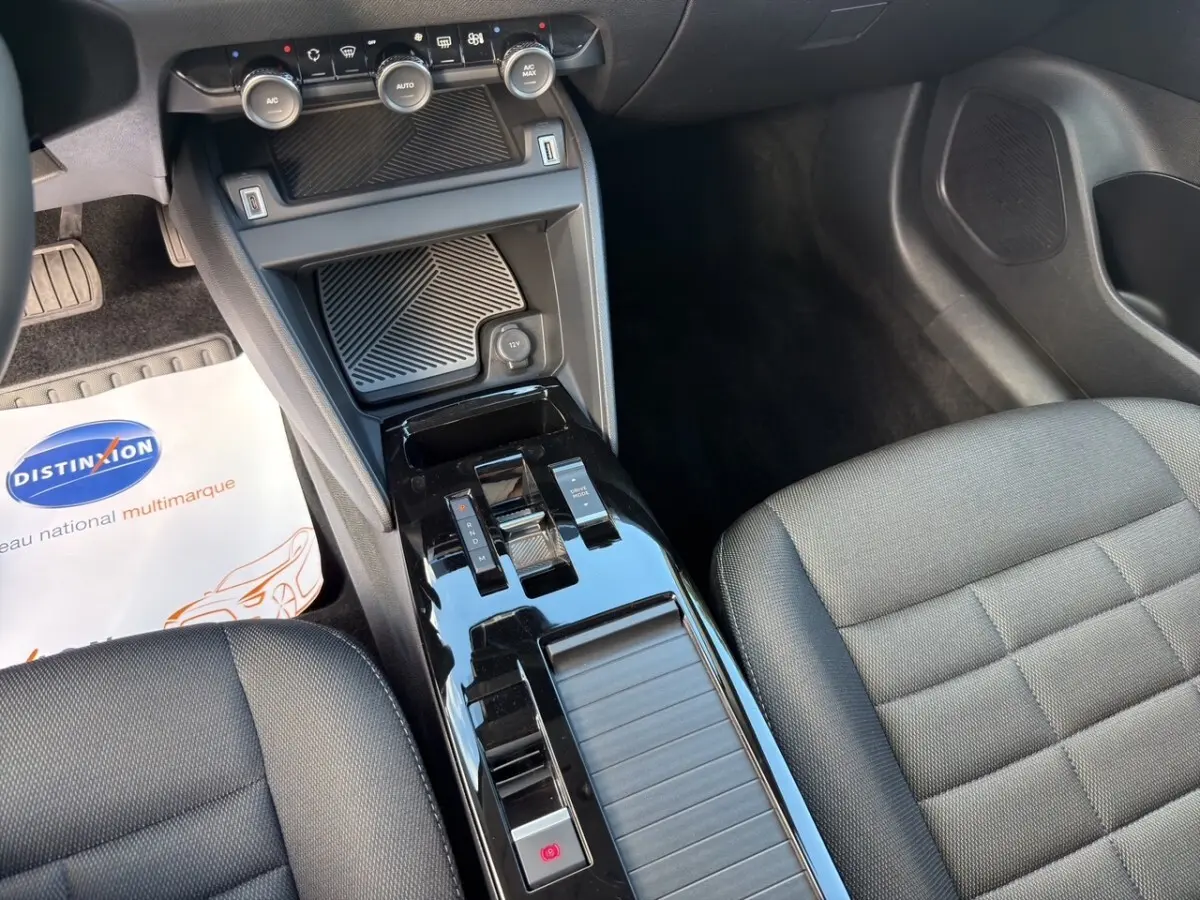 Vue intérieure centrée sur la console centrale noire brillante et les sièges tissu gris foncé d'une Citroën C4 hybride 2025.