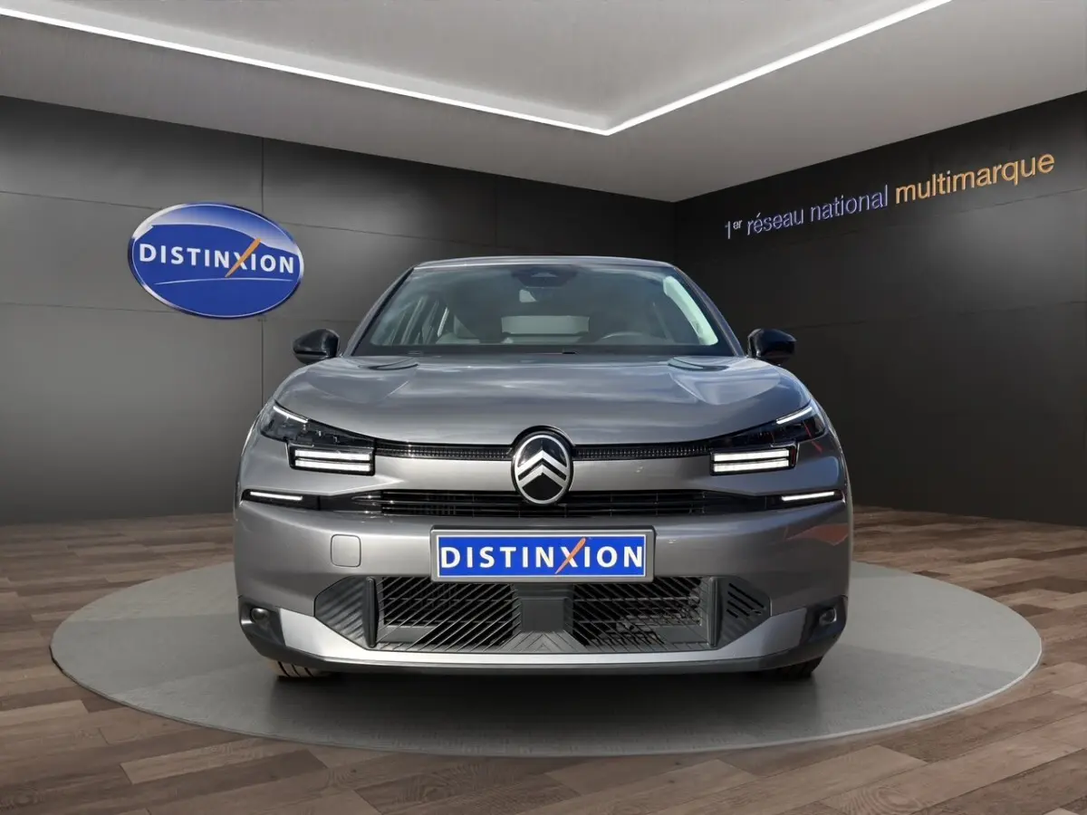 Vue frontale d'une Citroën C4 hybride gris foncé avec phares LED et calandre moderne en showroom.