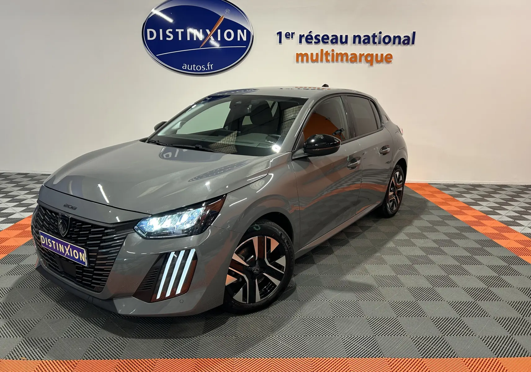 Peugeot 208 gris Selenium vue 3/4 avant droit avec phares LED allumés et jantes noires bicolores.