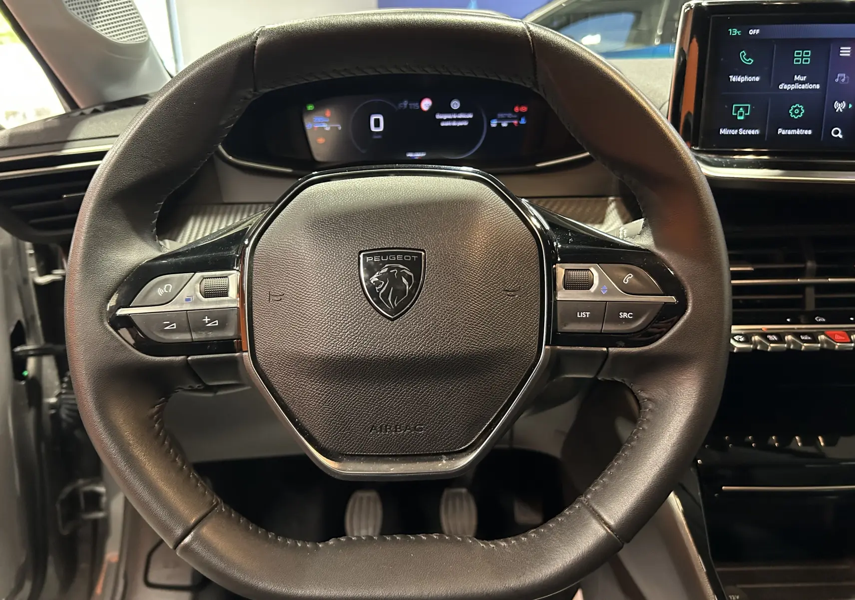 Vue centrée sur le volant cuir noir de la Peugeot 208 2025 avec tableau de bord numérique et écran tactile à droite.