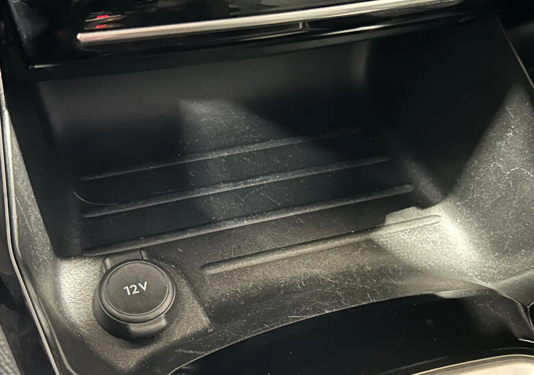 Gros plan sur la prise 12V et le rangement central noir intérieur de la Peugeot 208 gris Selenium, version 2025.