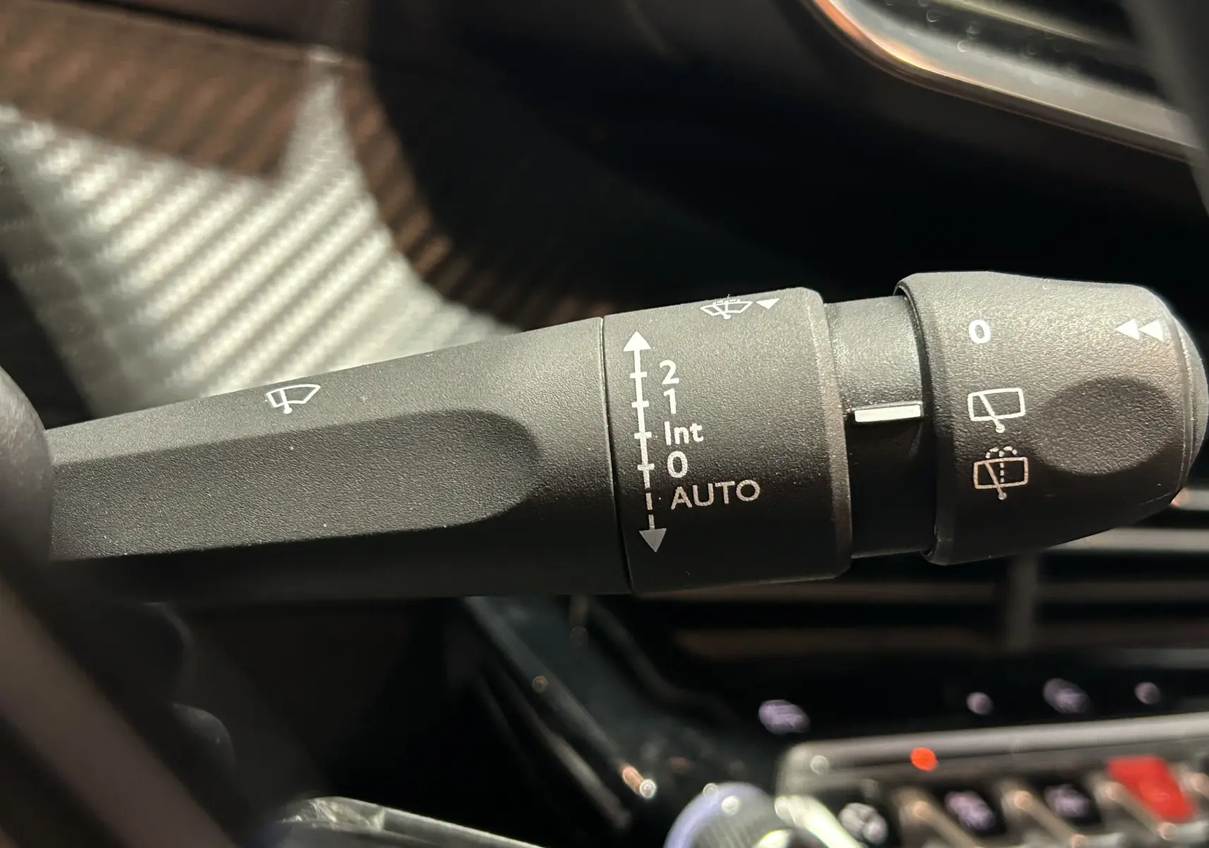 Gros plan sur la commande des essuie-glaces à gauche du volant dans l’habitacle d’une Peugeot 208 gris Selenium.