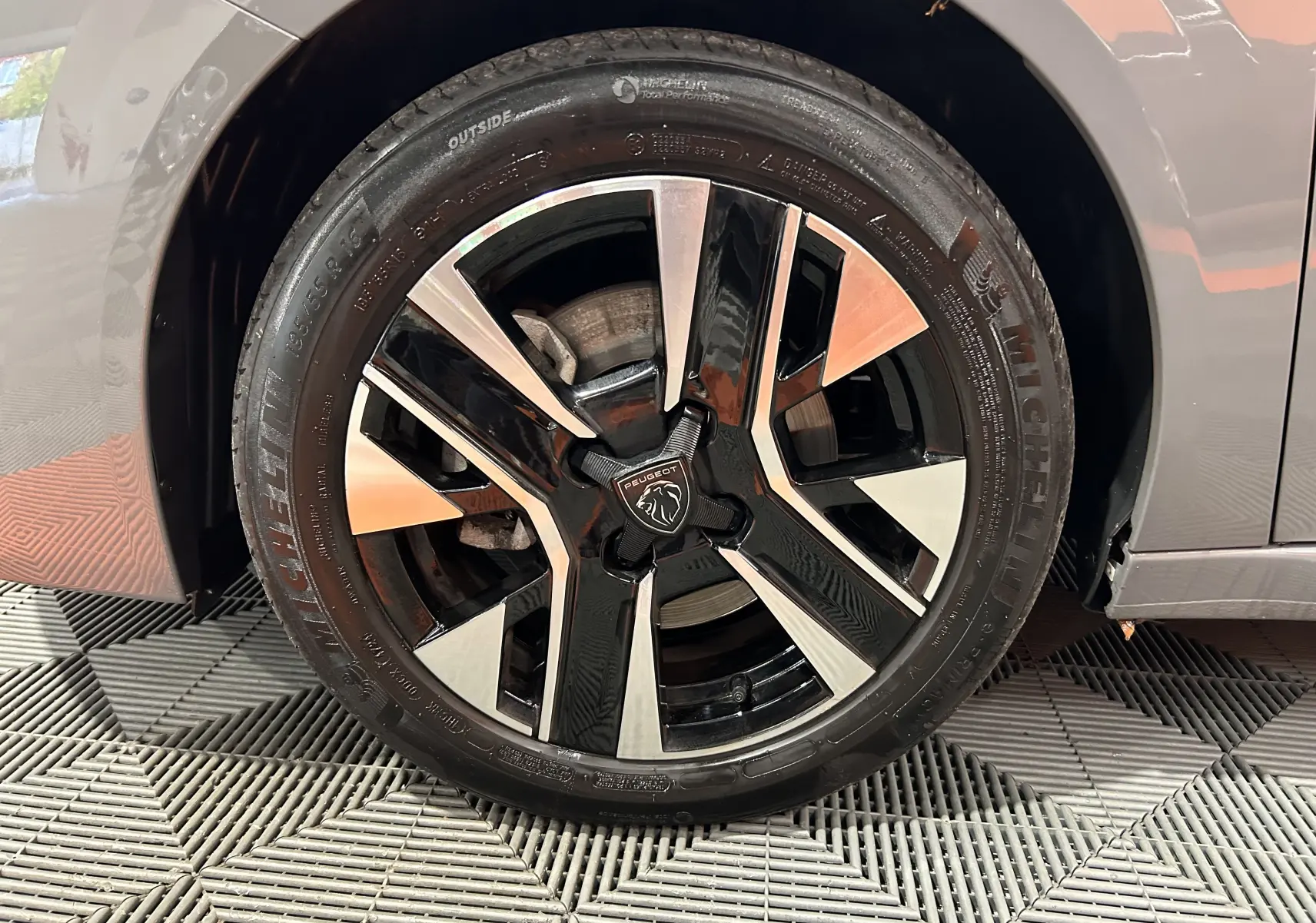 Gros plan sur la roue avant droite d’une Peugeot 208 gris Selenium, avec jante alliage noire et argentée au design moderne.