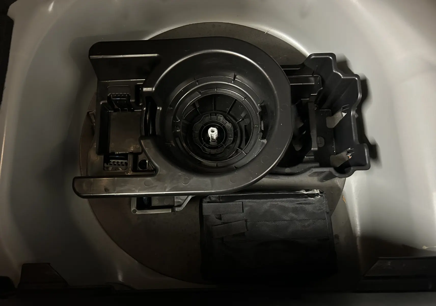 Gros plan sur le rangement sous le coffre d’un Peugeot 208 gris Selenium, montrant l’emplacement de la roue de secours et des outils.