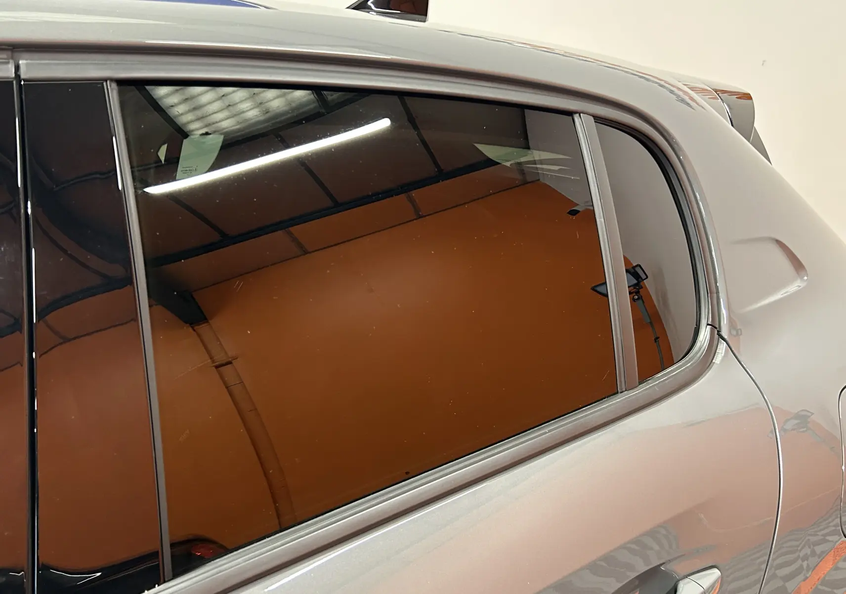 Gros plan sur la vitre arrière côté droit d'une Peugeot 208 gris Selenium, mettant en valeur la finition lisse et les contours chromés.