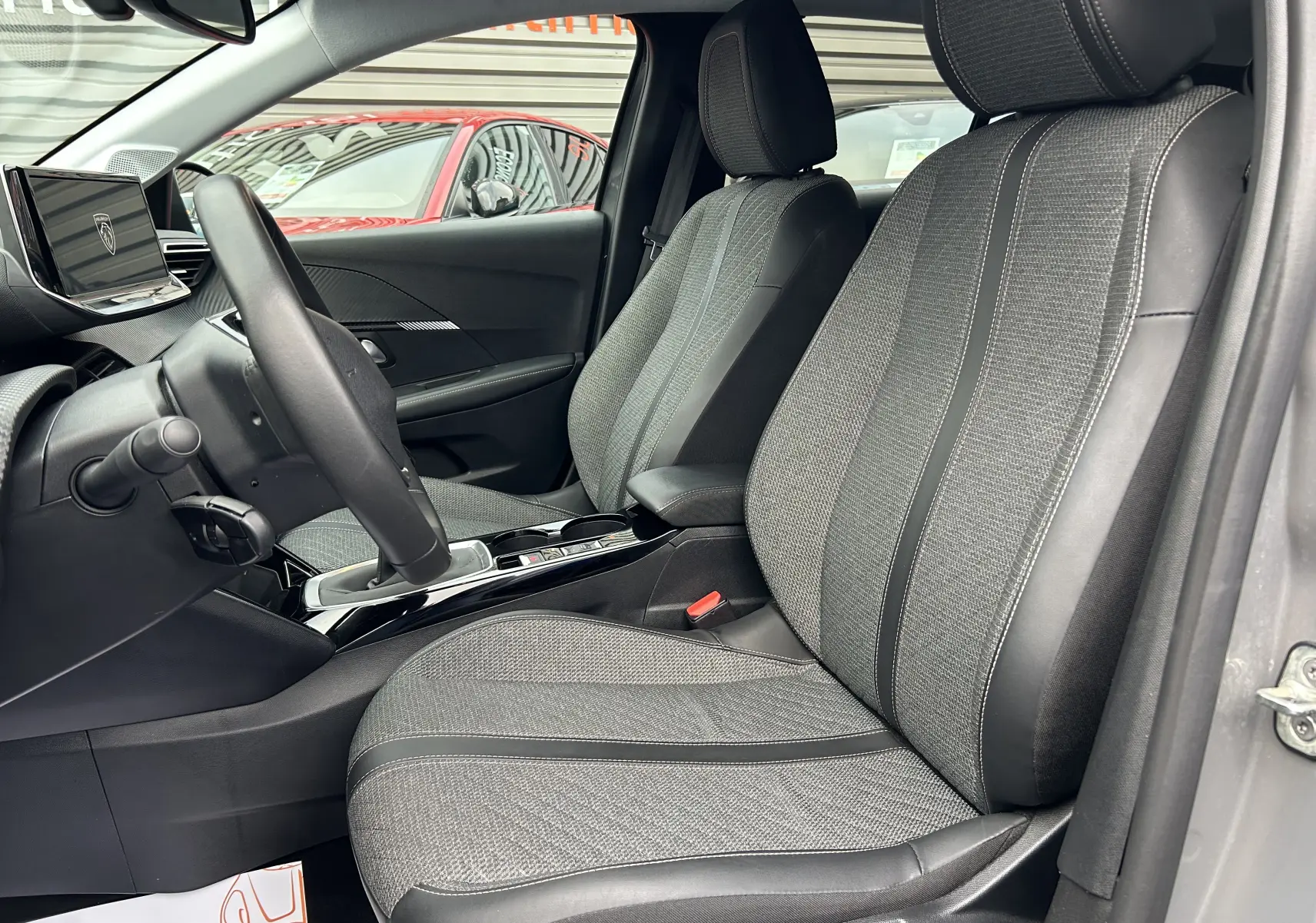 Vue intérieure côté conducteur de la Peugeot 208 gris Selenium, mettant en valeur les sièges tissu et cuir ainsi que la console centrale moderne.