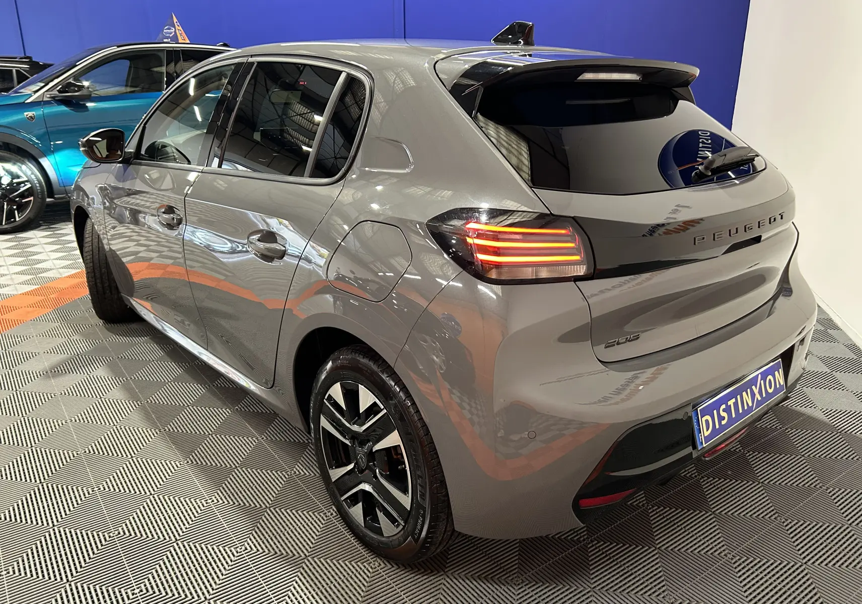 Peugeot 208 gris Selenium vue 3/4 arrière droit, feux arrière allumés et jantes noires distinctives.