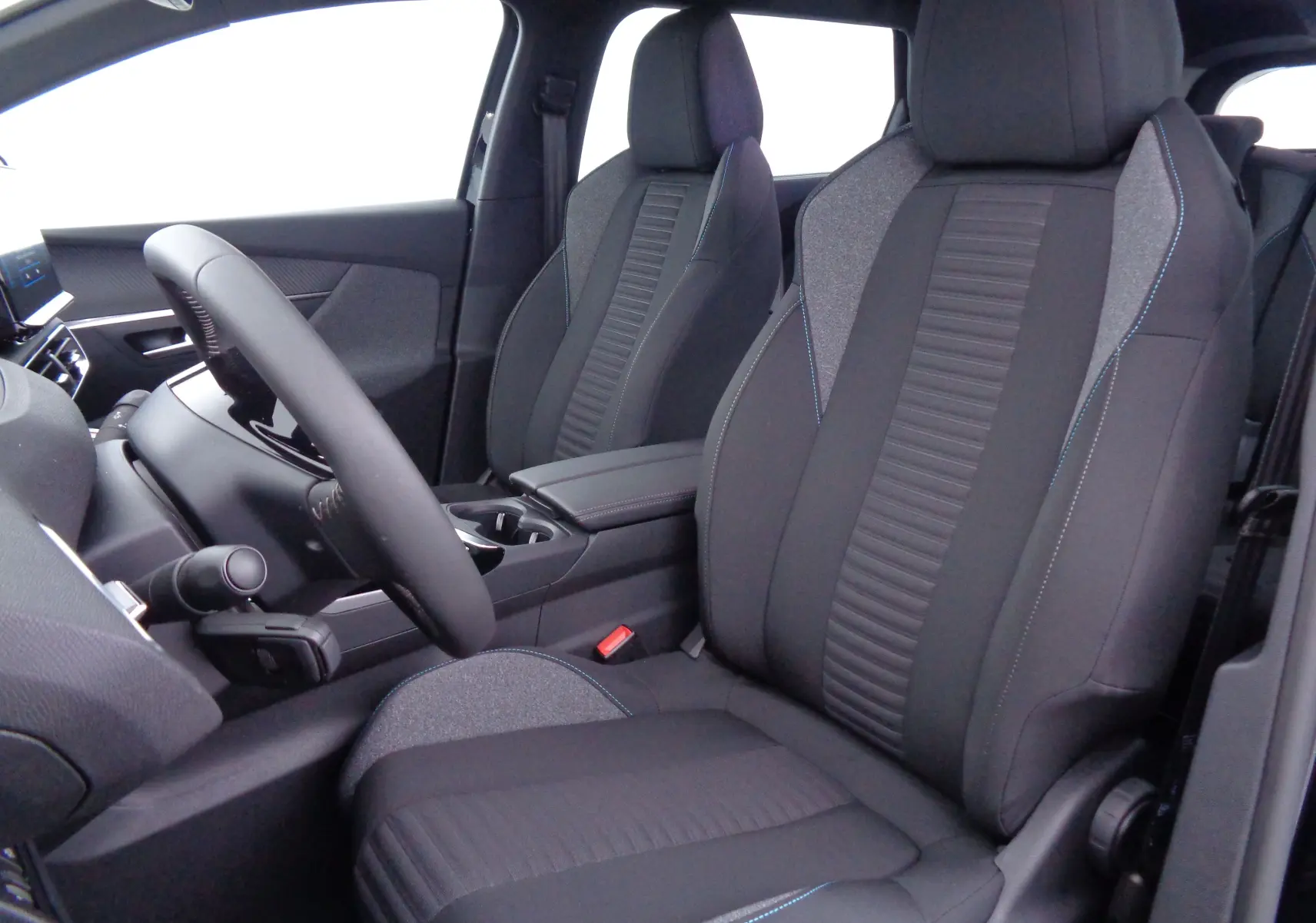 Intérieur avant du Peugeot 5008 2023, sièges tissu noir et gris avec surpiqûres bleues, volant et console centrale visibles.