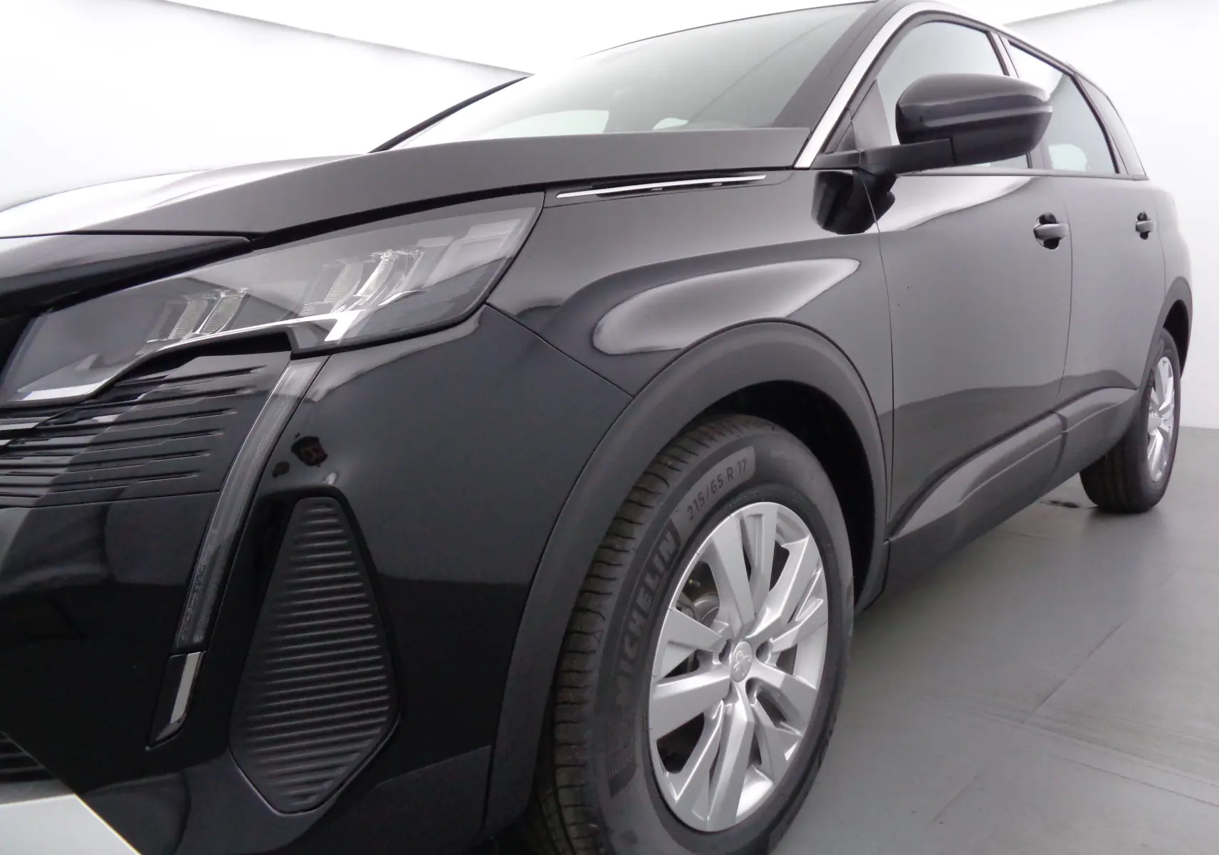 Vue 3/4 avant droit d'un Peugeot 5008 noir perle métal avec phares LED et jantes alliage 17 pouces.
