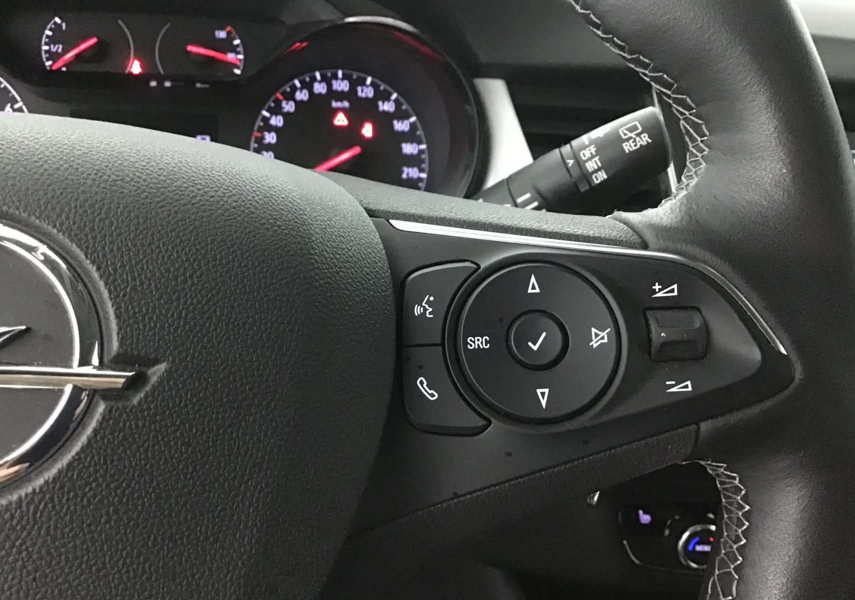 Gros plan sur le volant côté gauche de l'Opel Crossland noir 2022, avec commandes audio et tableau de bord éclairé en arrière-plan.