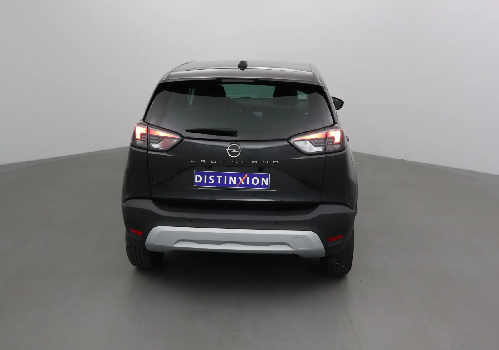Vue arrière d'un Opel Crossland noir 2022 avec feux allumés et plaque Distinxion visible sur fond neutre.