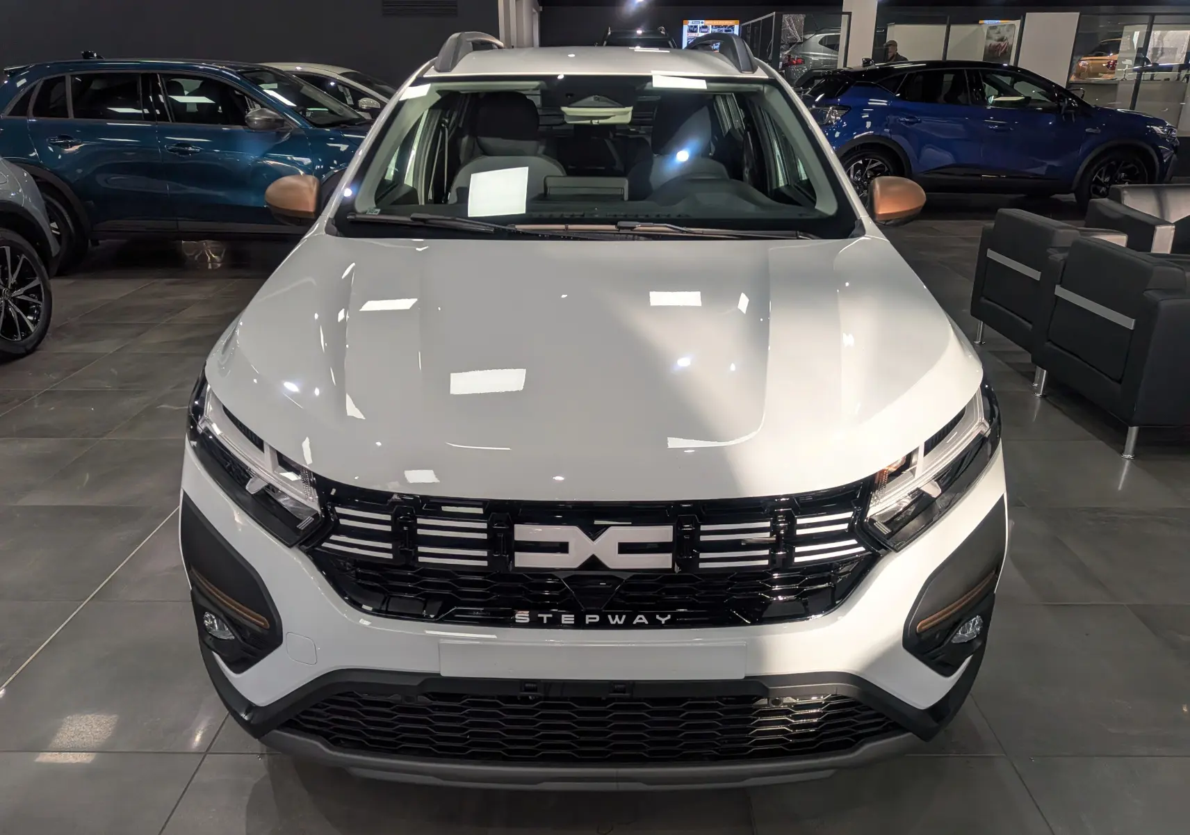 Vue frontale d'une Dacia Sandero Stepway blanc glacier en showroom, avec calandre noire et détails bronze sur les phares.