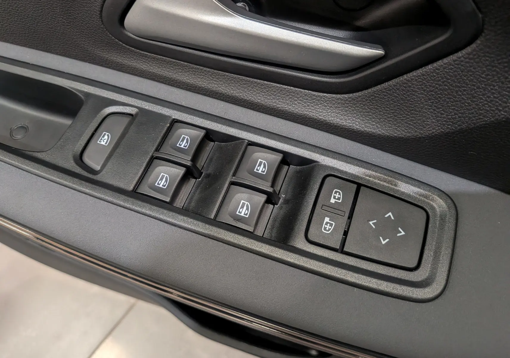 Gros plan sur les commandes de lève-vitres et réglage des rétroviseurs côté conducteur d'une Dacia Sandero Stepway TCe 110 Blanc Glacier.