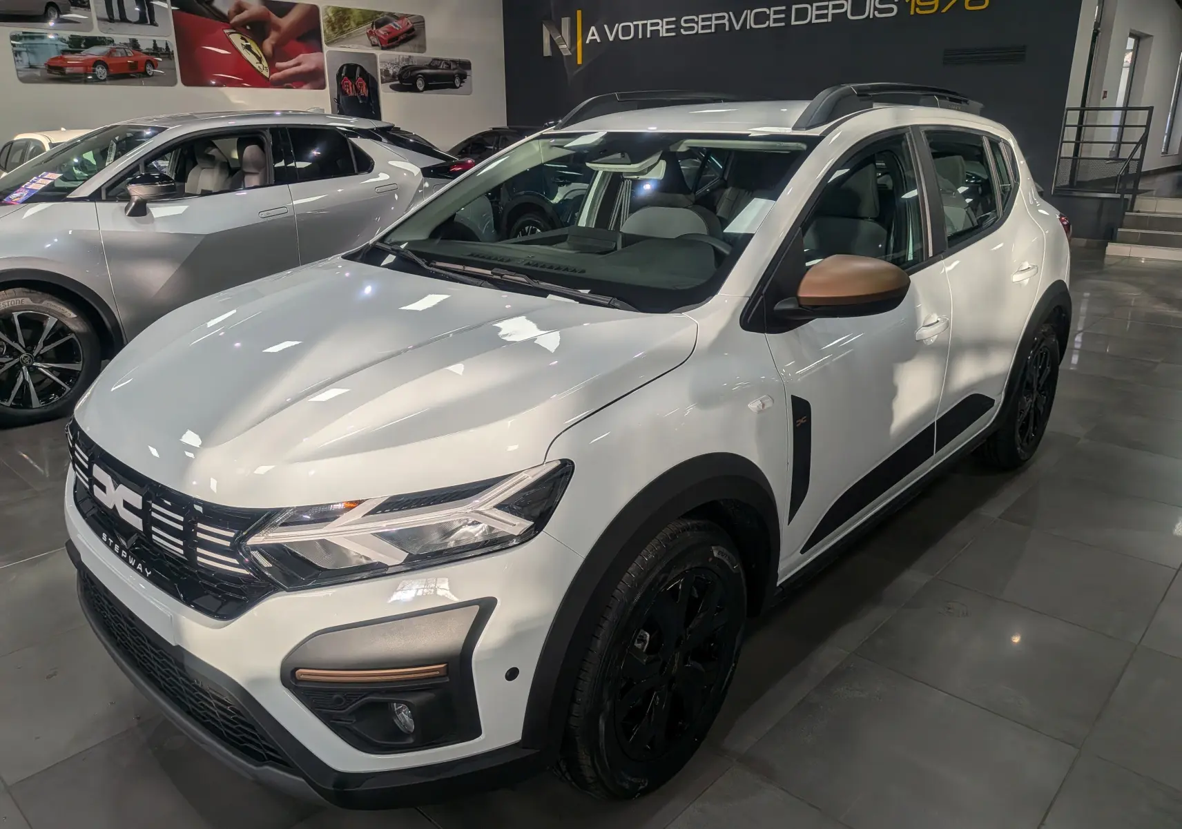 Vue 3/4 avant droit d'une Dacia Sandero Stepway TCe 110 blanc glacier avec rétroviseurs bronze et jantes noires en showroom.