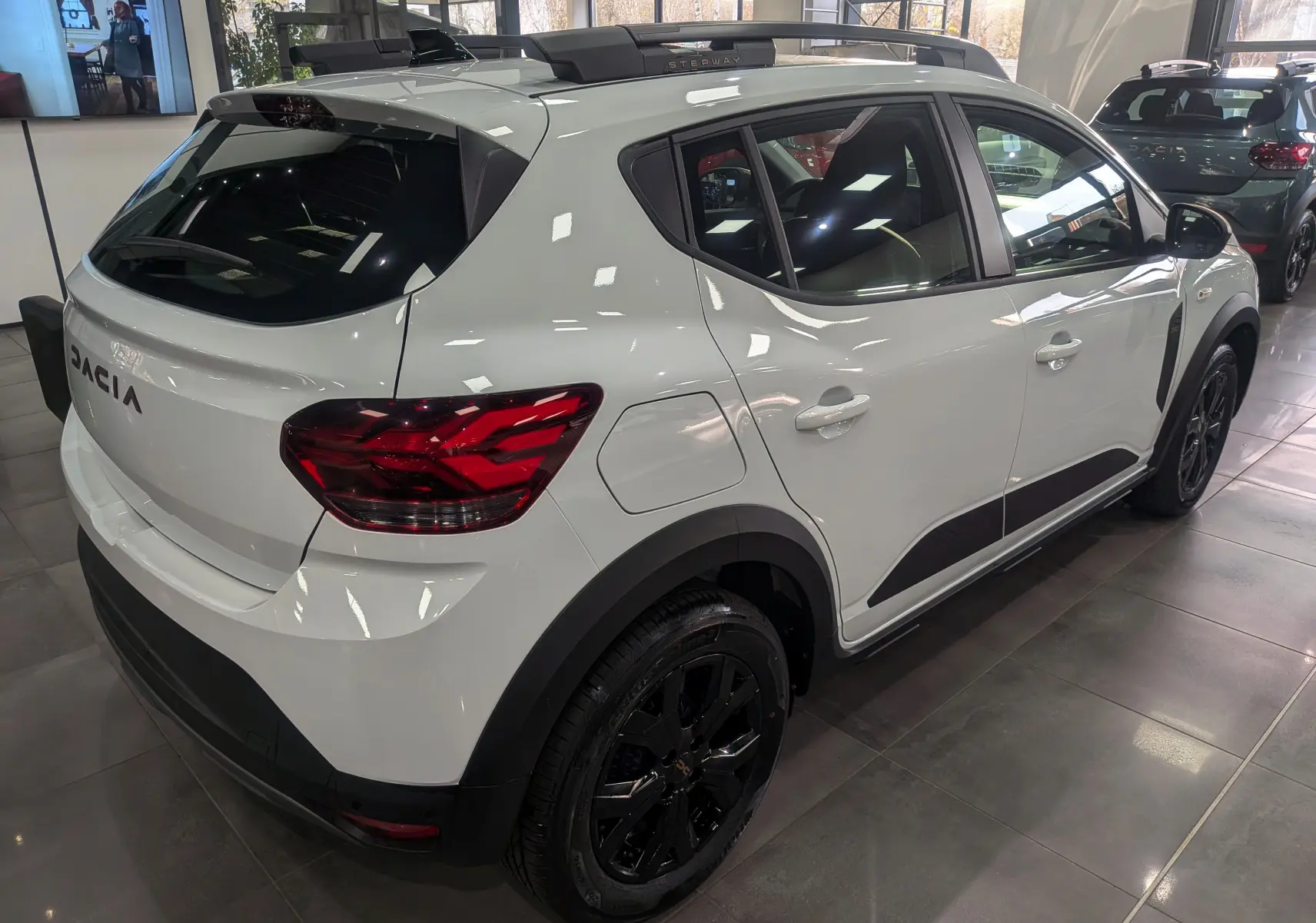 Vue côté droit d'une Dacia Sandero Stepway TCe 110 blanche Glacier avec jantes noires en showroom.